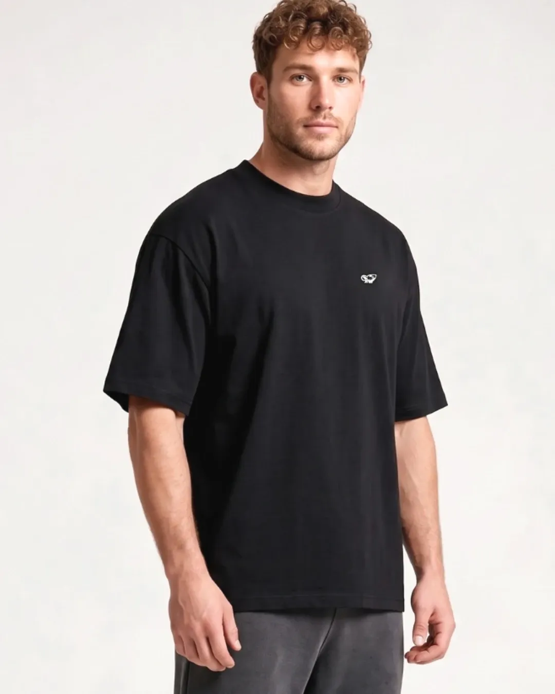 Male model wearing the black SQUATRAT SR-T-003 minimalist oversized T-shirt, front detail with small chest logo.